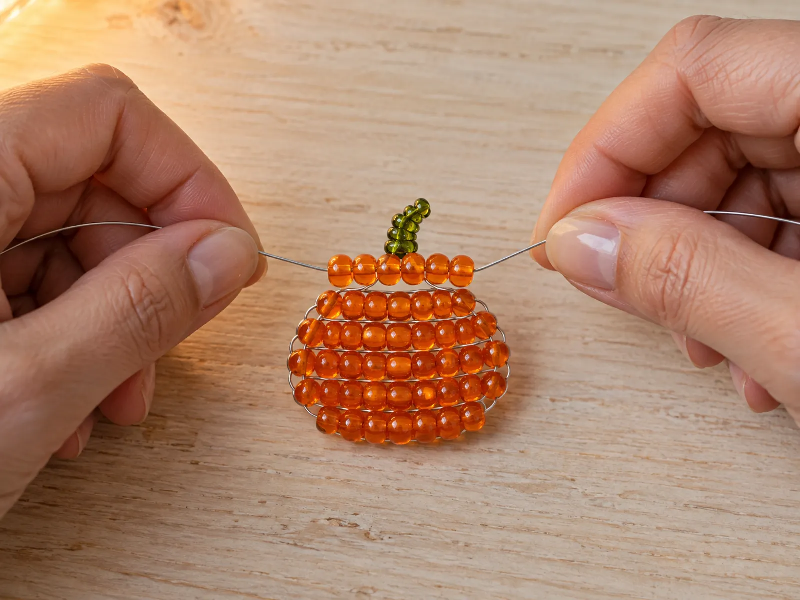 KI-generiertes Bild: Hände kreuzen Silberdraht durch eine Reihe orangefarbener Glasperlen an einem halbfertigen Kürbisanhänger